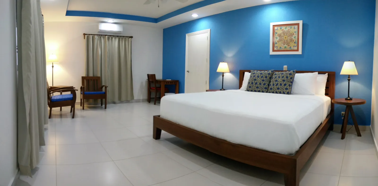 The Deluxe King room: a king bed against a cobalt-blue wall, bedside lamps, armchairs and curtained windows