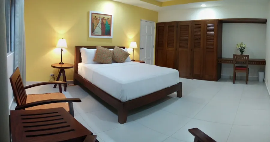 A queen room with a yellow wall, wooden bed, desk and a wall of louvred closets